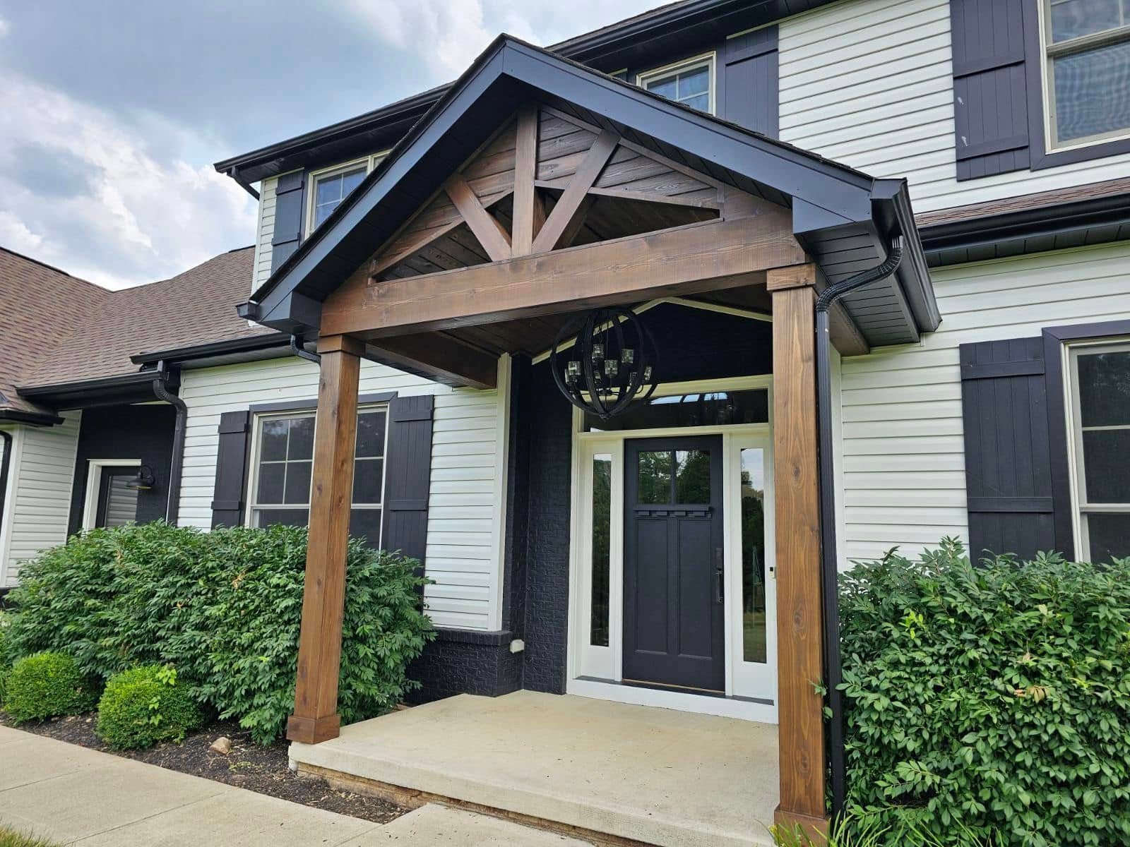 Timber-frame portico with a truss gable and stained posts over a dark craftsman front door
