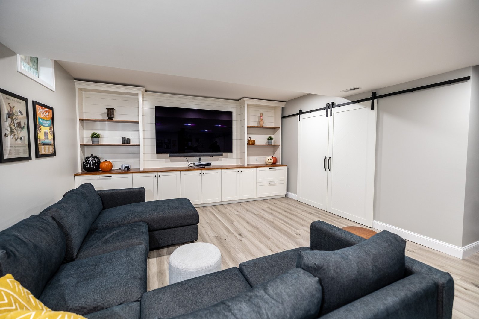 Basement media wall with built-in white cabinetry, shiplap panelling, floating wood shelves and barn doors