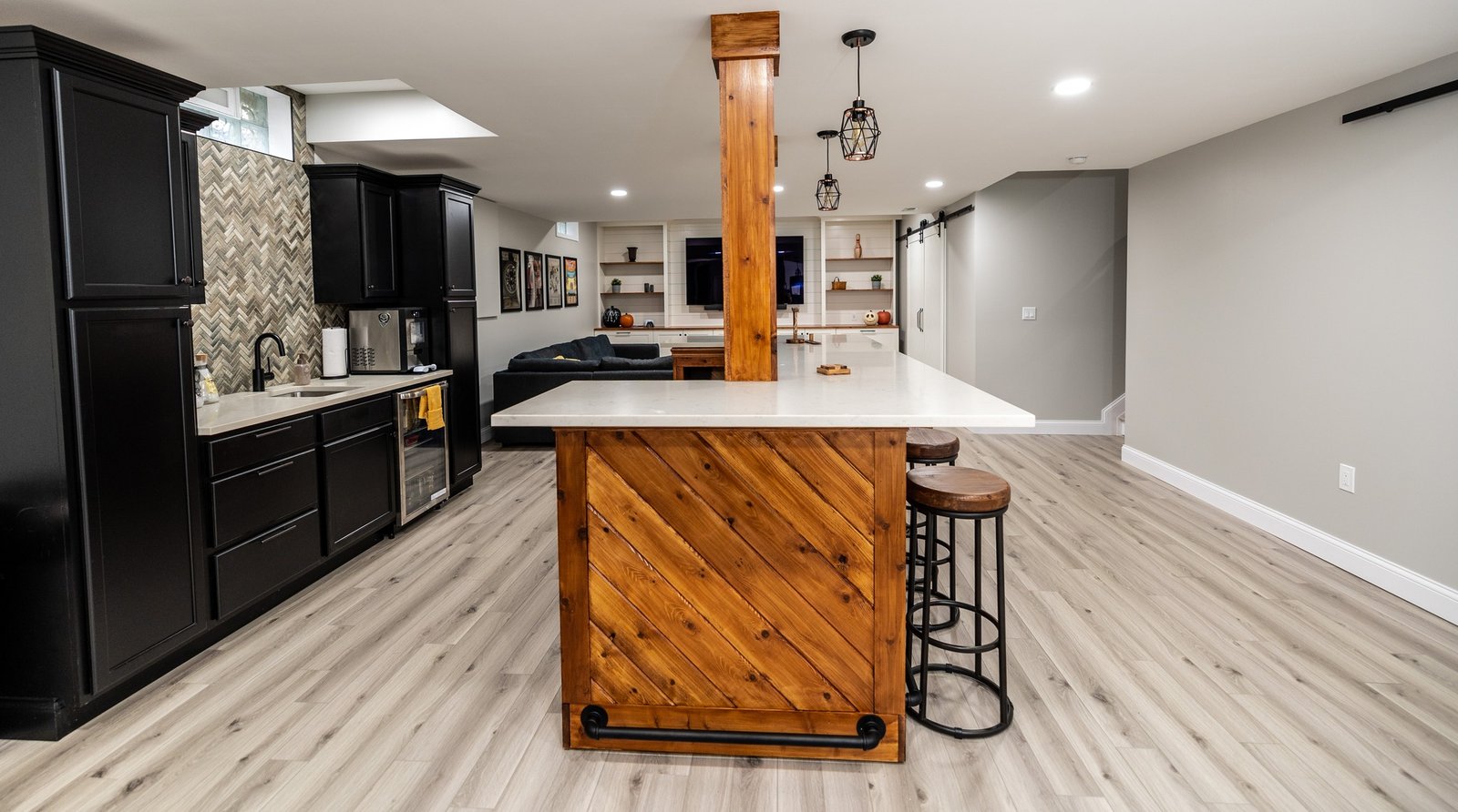 Wide view of a finished basement with a chevron-clad cedar bar, quartz top and a black kitchenette behind it