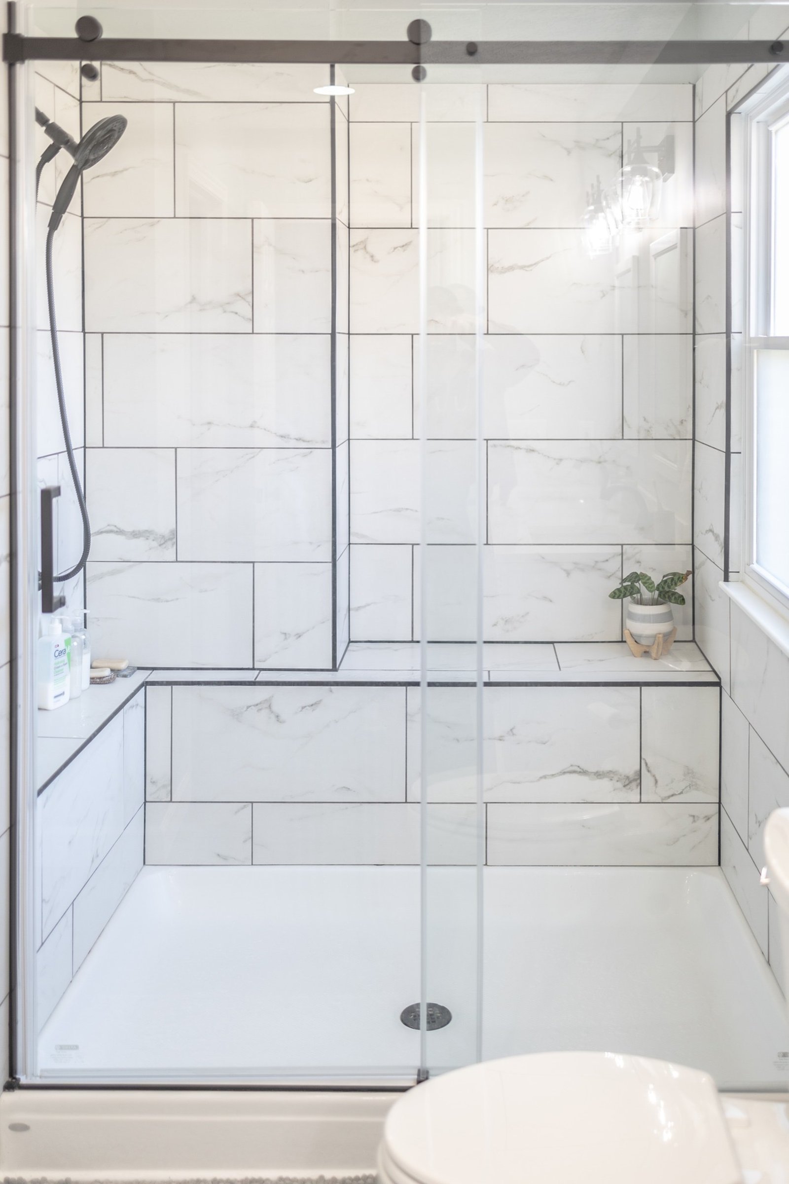 Walk-in shower tiled in large-format marble-look porcelain with dark grout and matte black fixtures
